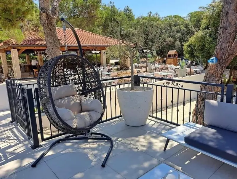 Un fauteuil suspendu sur une terrasse ensoleillée avec des tables et des chaises.