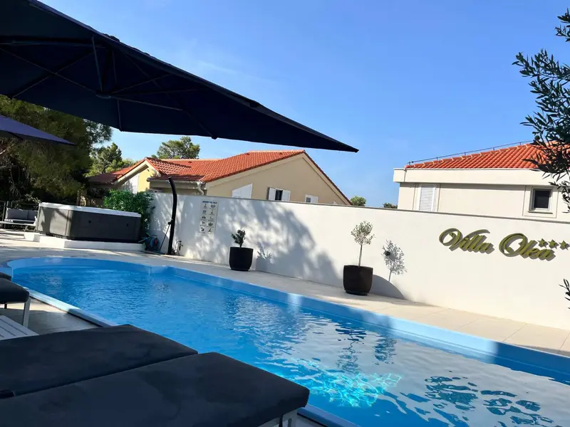 Piscine rectangulaire avec transats et parasols près d'une maison blanche.