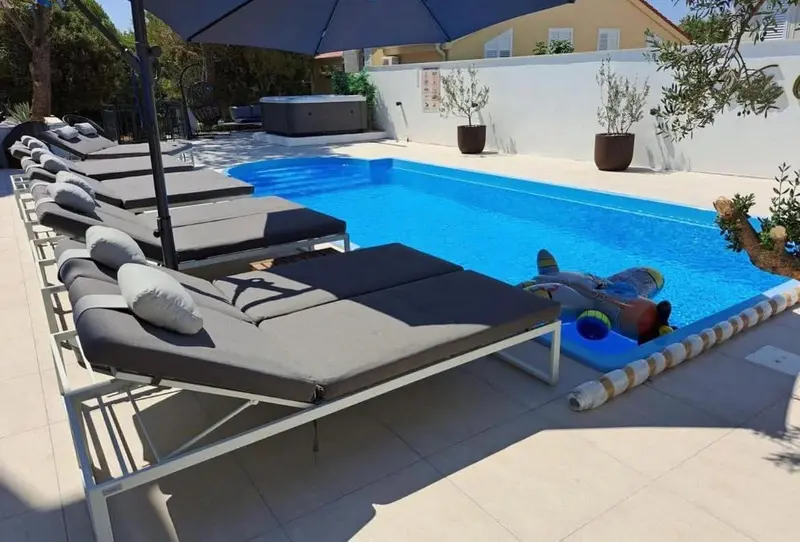 Transats gris et piscine bleue au bord d'une terrasse ensoleillée.