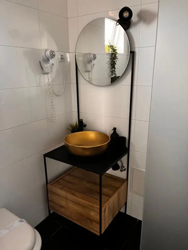 Une salle de bain moderne avec un lavabo doré et des murs carrelés blancs.