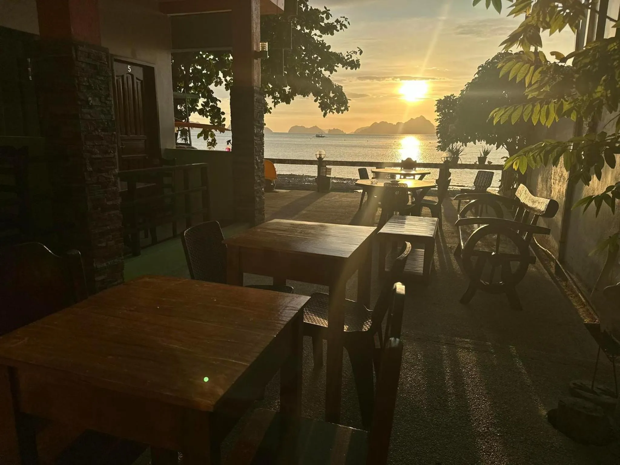 Terrasse avec tables et chaises face à la mer au coucher du soleil.