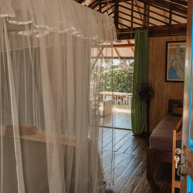 Une chambre avec un lit recouvert d'une moustiquaire donne sur une terrasse en bois.