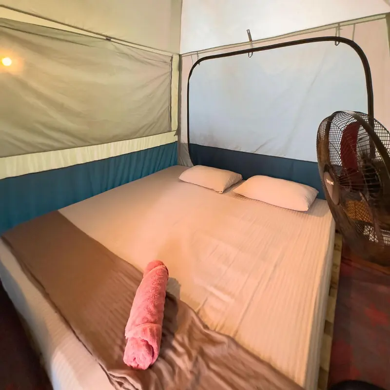 Un lit simple dans une tente avec un oreiller et une serviette rose.