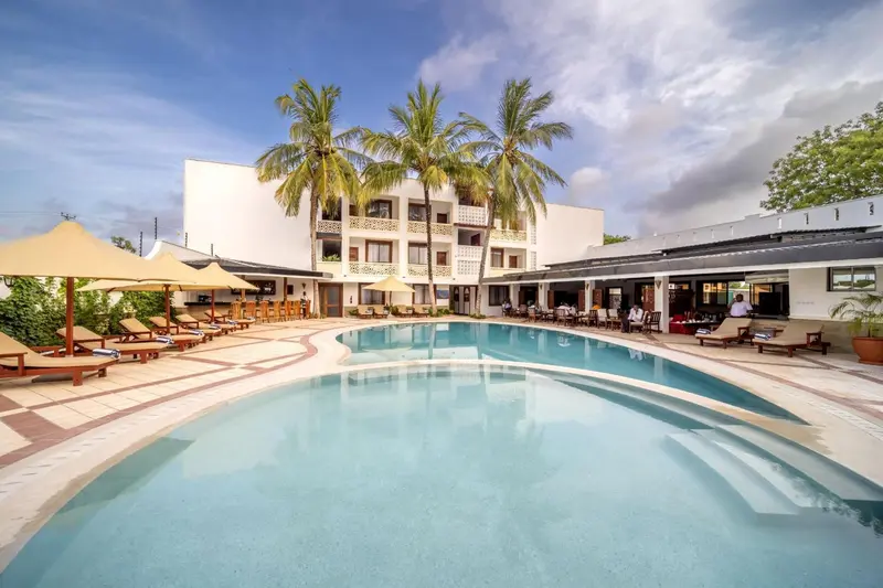 Une piscine turquoise reflète un bâtiment blanc bordé de palmiers sous un ciel bleu.