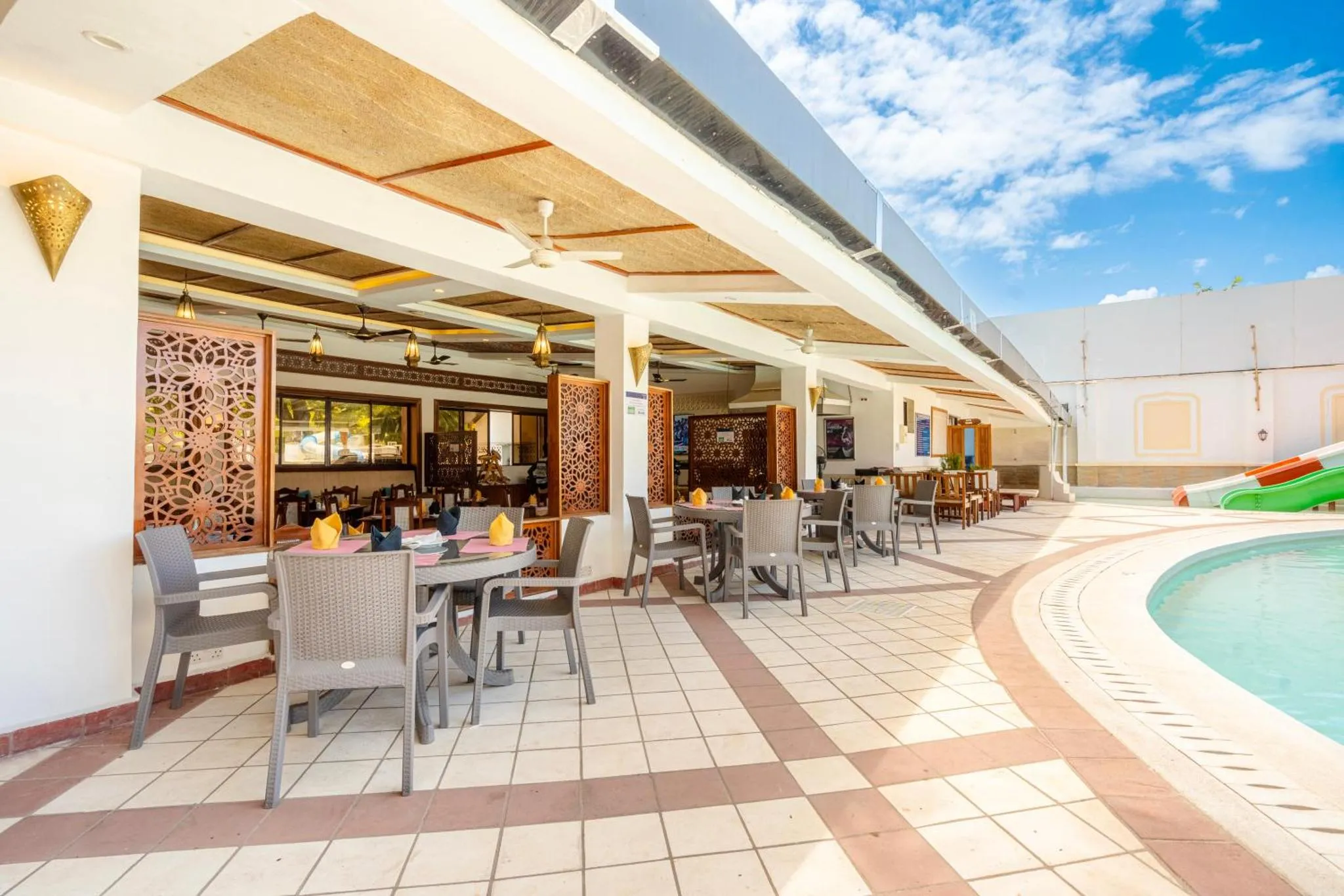 Terrasse ombragée avec tables et chaises près d'une piscine.
