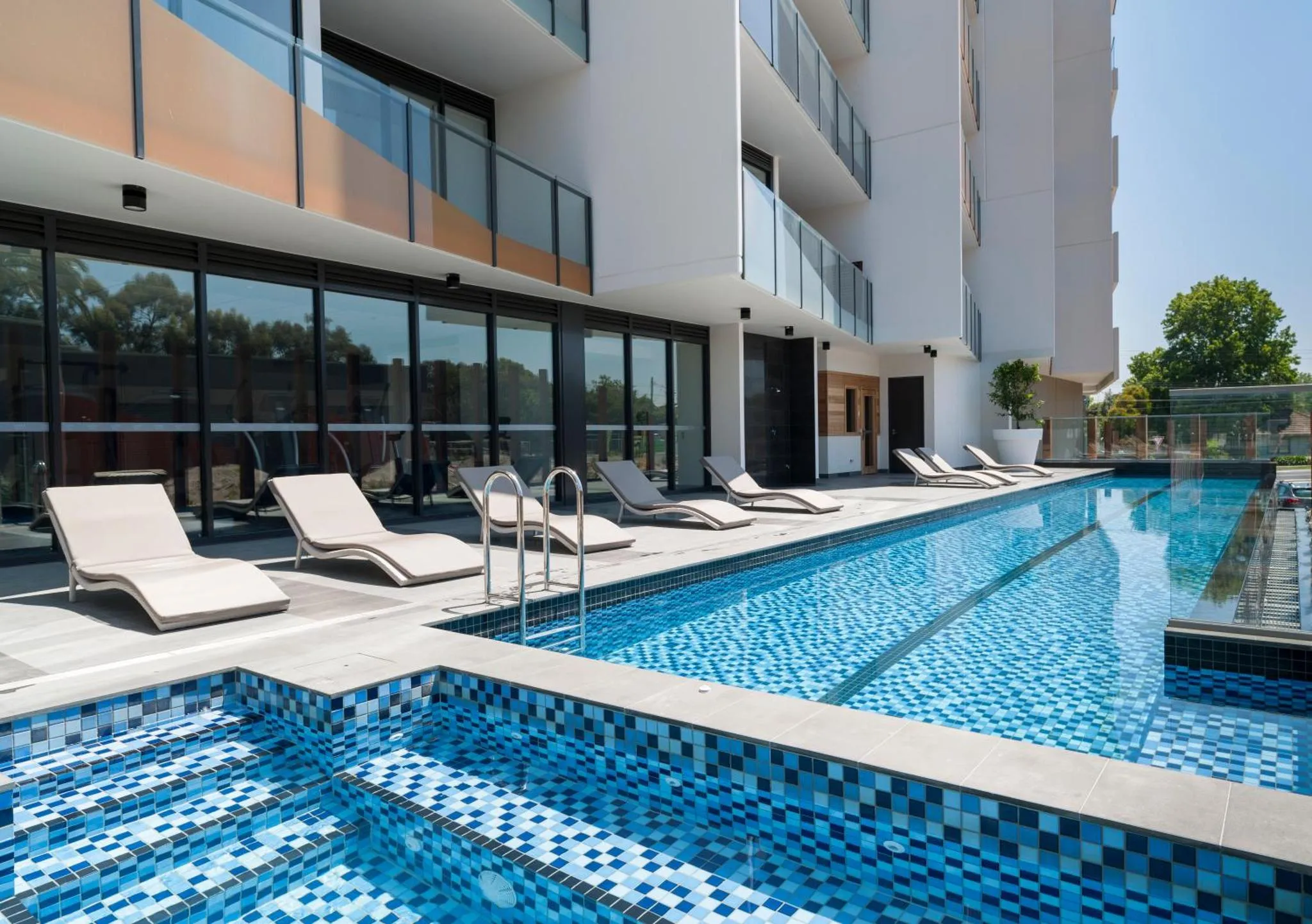 Transats alignés au bord d'une piscine rectangulaire carrelée.