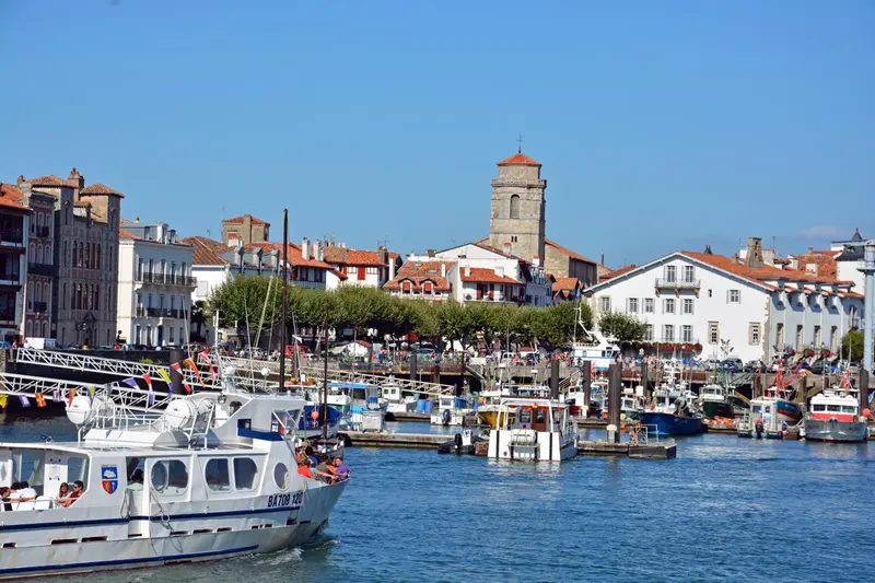 Port de plaisance ensoleillé avec des bateaux amarrés et une ville en arrière-plan.