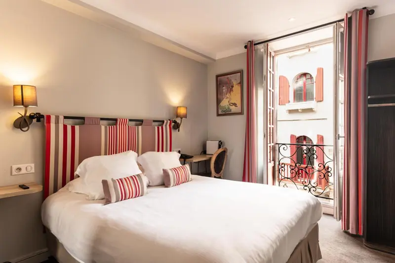 Une chambre lumineuse avec un lit double et un balcon en fer forgé.