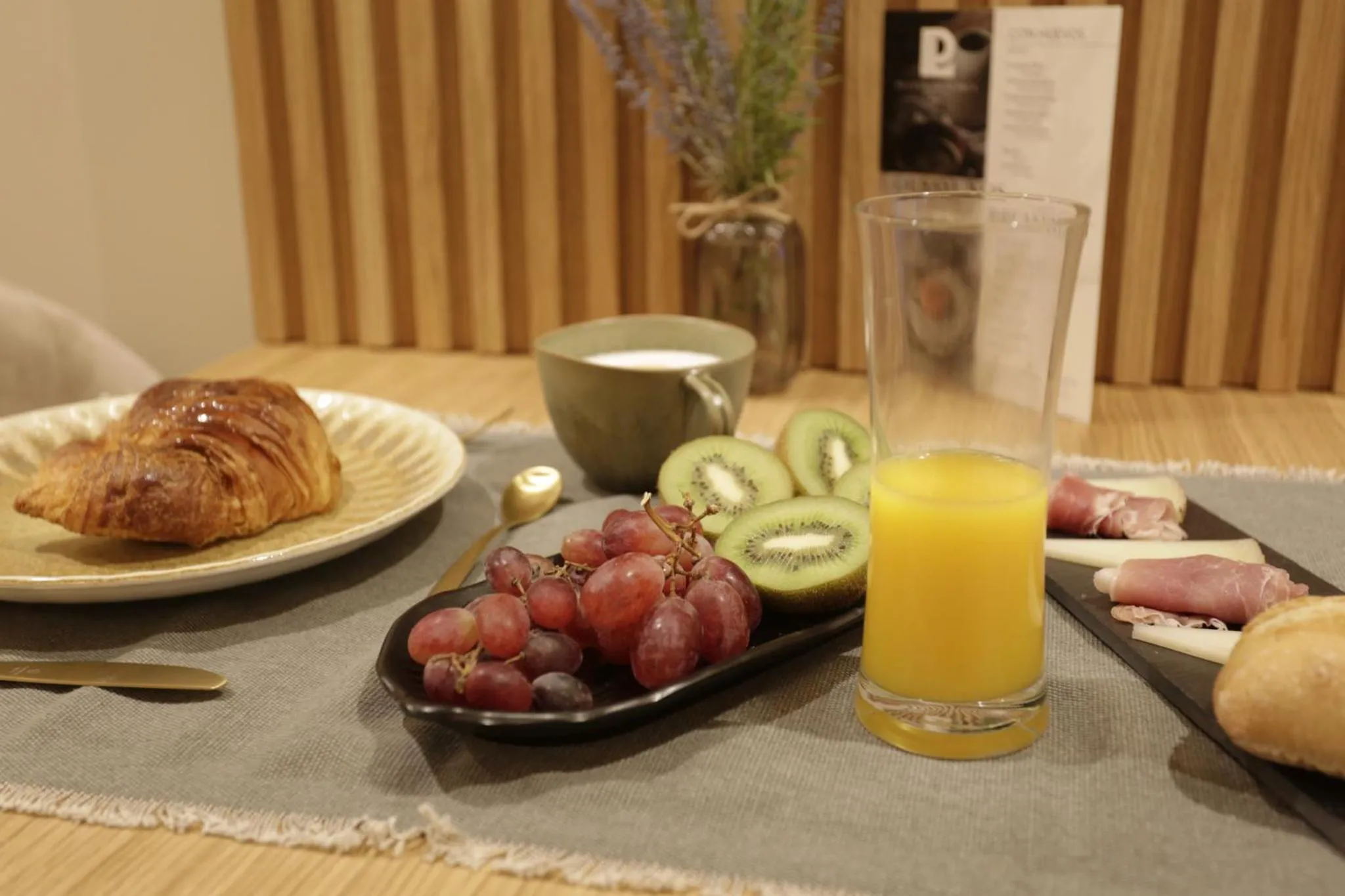 Une table en bois présente un petit-déjeuner avec des viennoiseries, des fruits et des boissons.