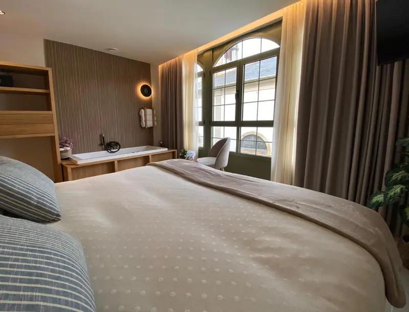 Une chambre lumineuse avec un grand lit et une baignoire près de la fenêtre.