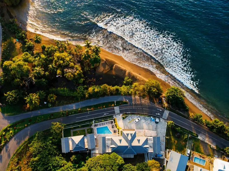 Vue aérienne d'une plage bordée de végétation et d'un bâtiment avec une piscine.