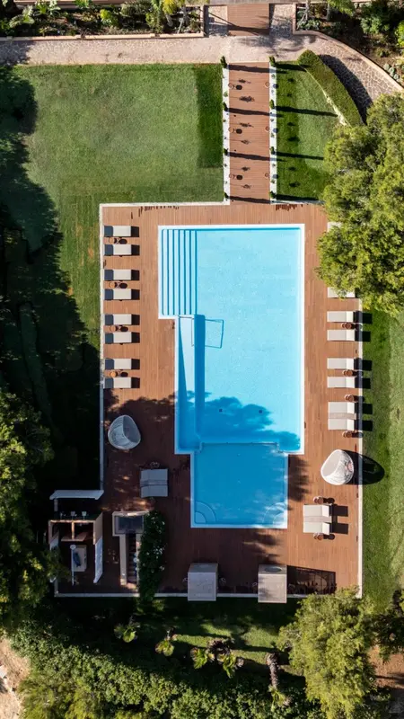 Vue aérienne d'une piscine rectangulaire entourée d'une terrasse en bois et de chaises longues.