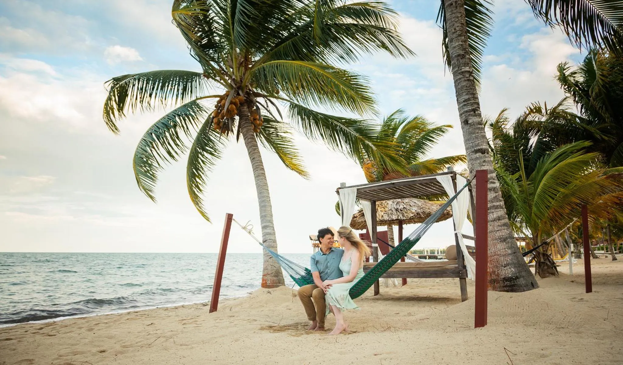 Un couple se détend dans un hamac sur une plage de sable fin bordée de palmiers.