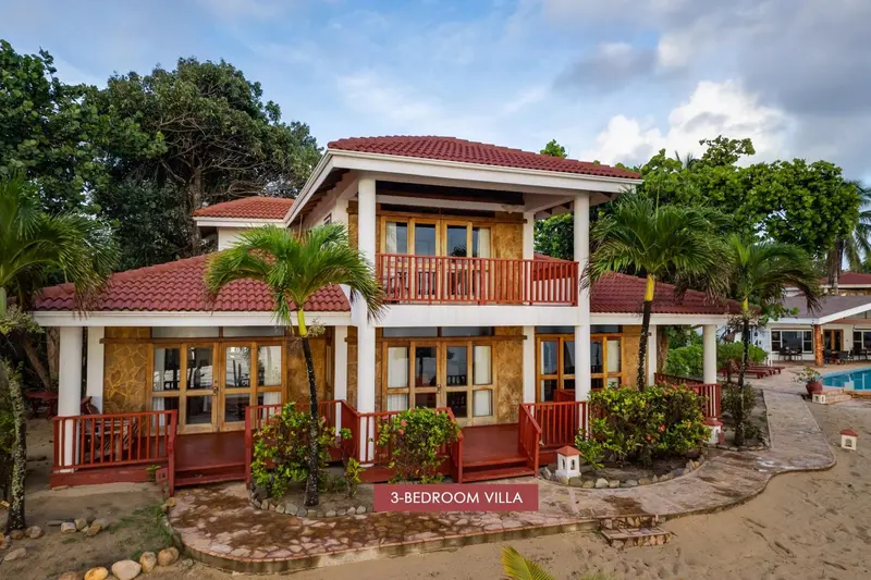 Villa blanche avec toiture rouge et végétation tropicale.