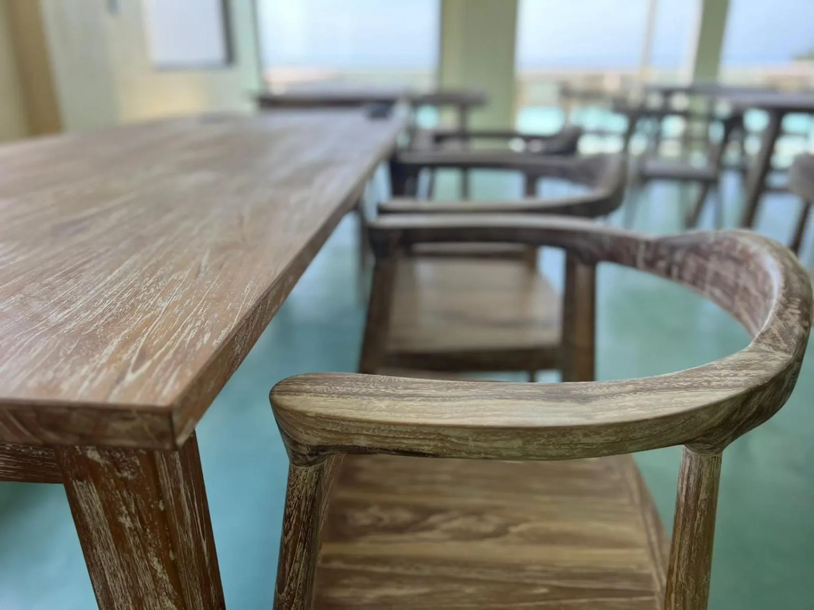 Une table en bois clair et des chaises en osier sont disposées dans une salle lumineuse.