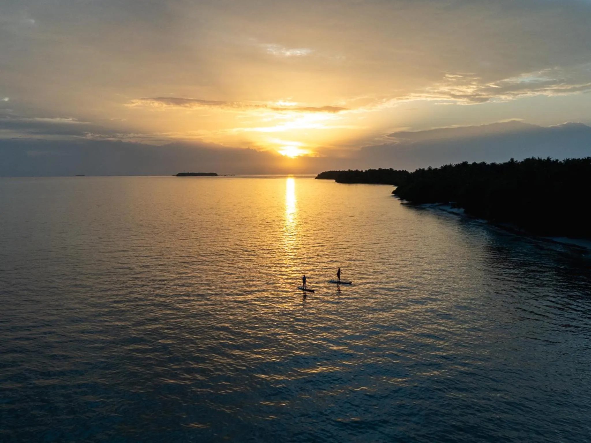 Coucher de soleil sur l'océan avec deux silhouettes pratiquant le paddleboard.