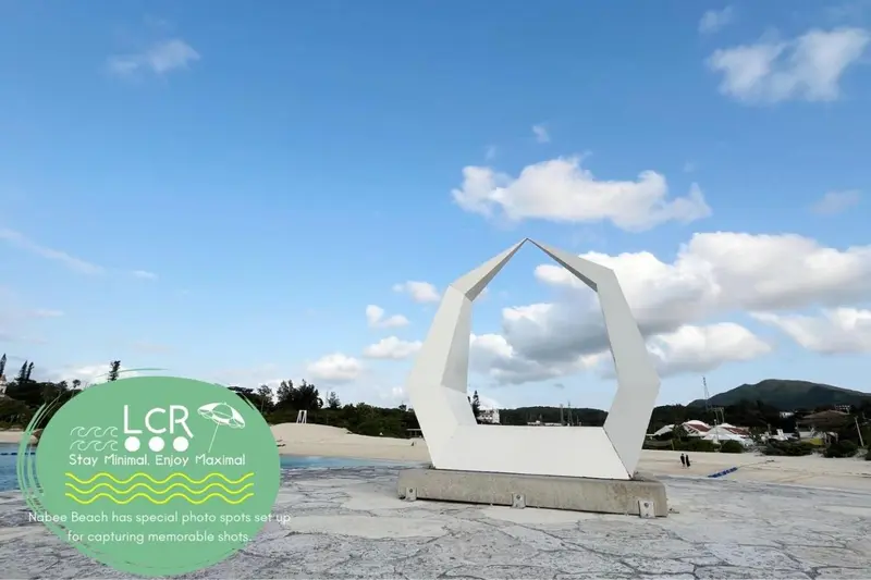 Sculpture blanche moderne sur une plage de sable clair sous un ciel nuageux.