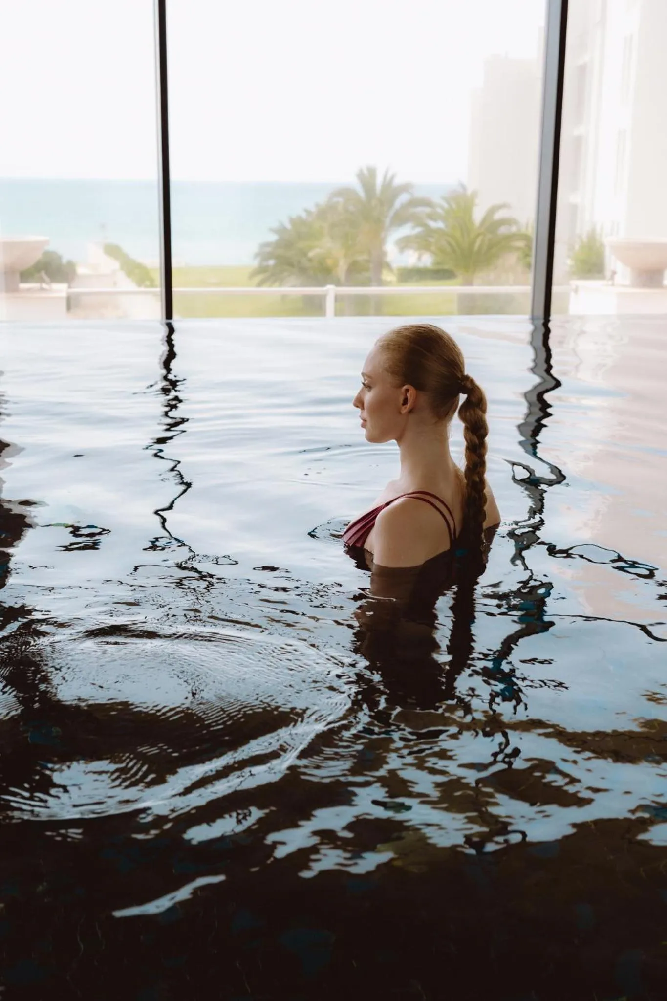 Une femme se tient dans une piscine intérieure avec vue sur la mer.