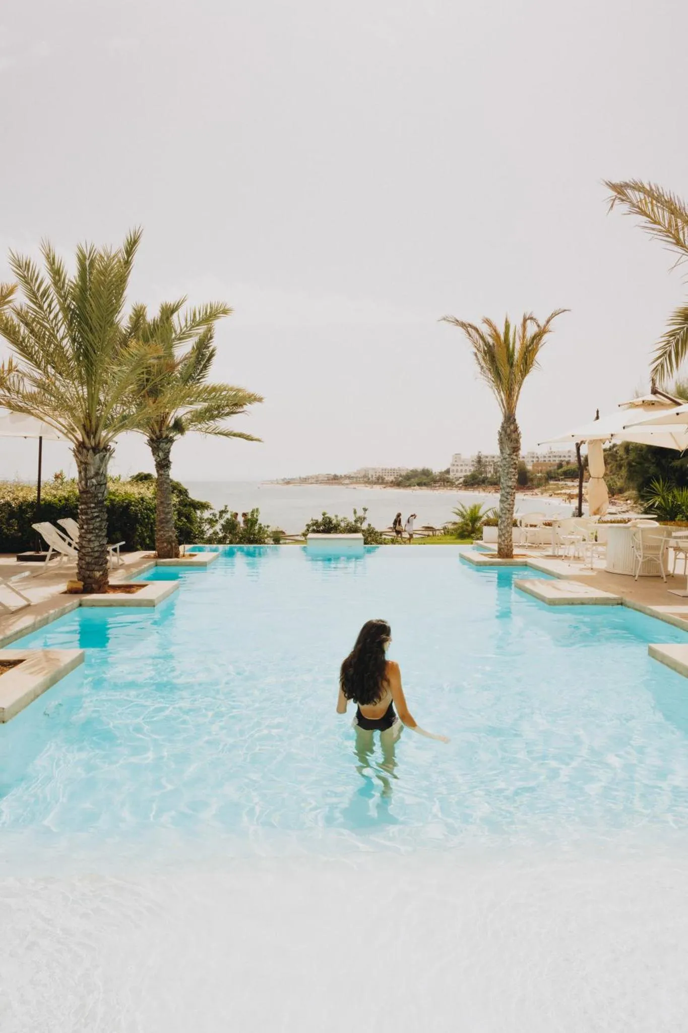 Une personne se tient dans une piscine à débordement avec vue sur la mer.