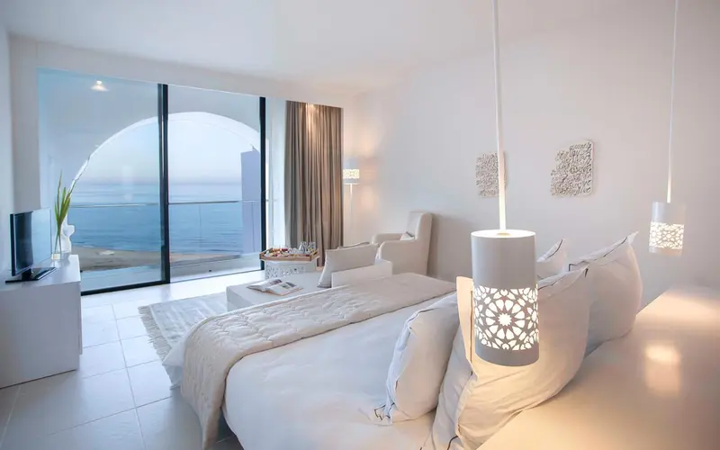 Chambre lumineuse avec un grand lit et vue sur la mer.