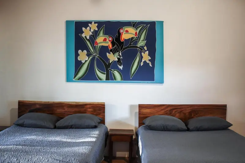 Deux lits simples avec oreillers dans une chambre décorée d'une grande toile représentant des toucans.
