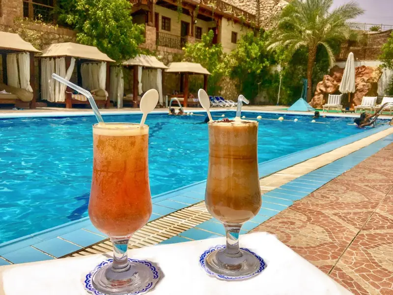 Deux cocktails colorés sont posés au bord d'une piscine ensoleillée.