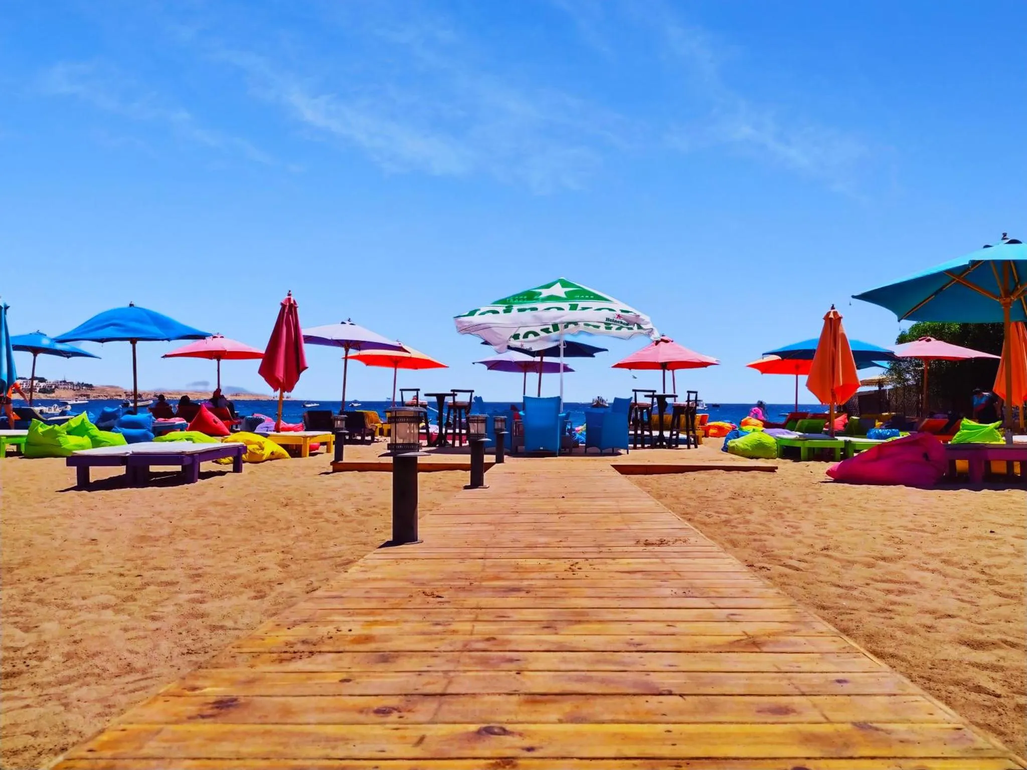 Plage de sable avec transats et parasols colorés face à la mer.