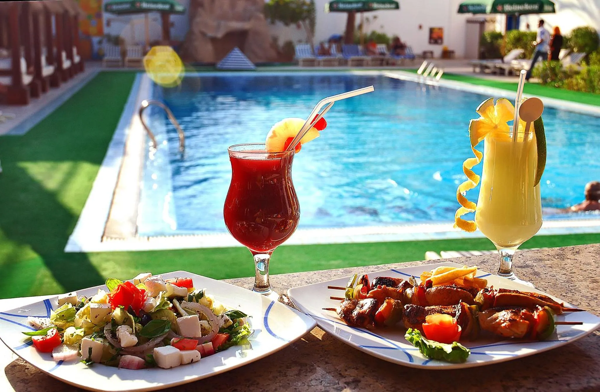 Des plats et des boissons colorées sont servis en bord de piscine.