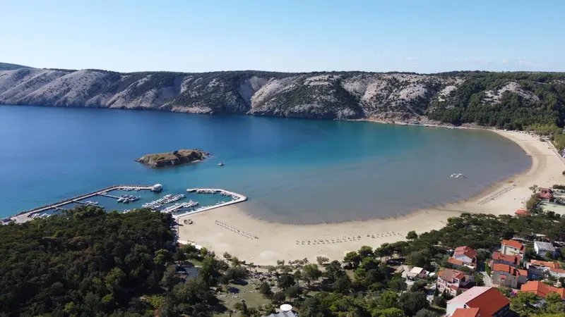 Vue aérienne d'une plage de sable fin bordée d'une eau turquoise et d'une végétation verdoyante.