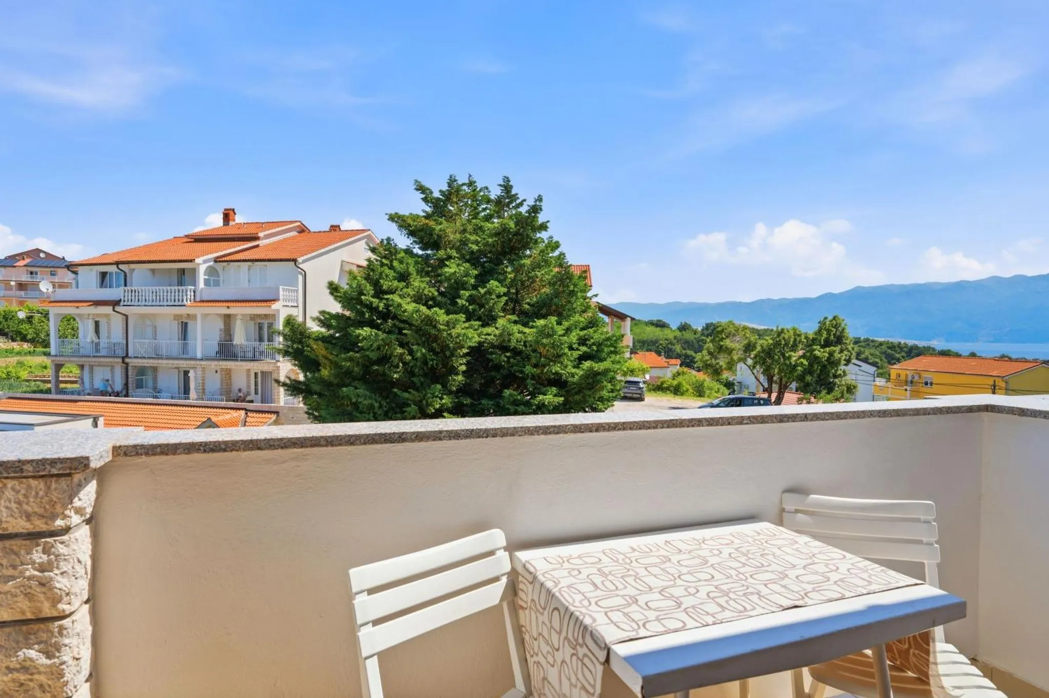 Une terrasse avec une table et des chaises offre une vue sur la mer et les bâtiments environnants.