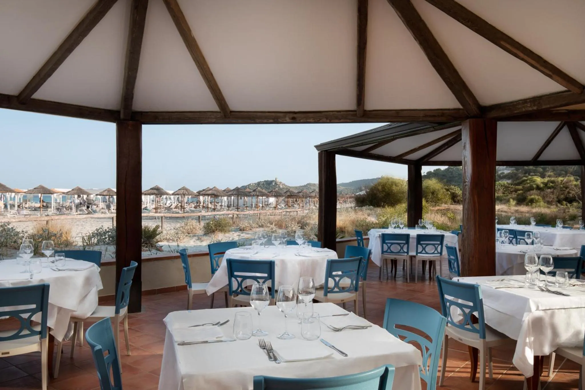 Terrasse ombragée avec tables dressées face à la mer.