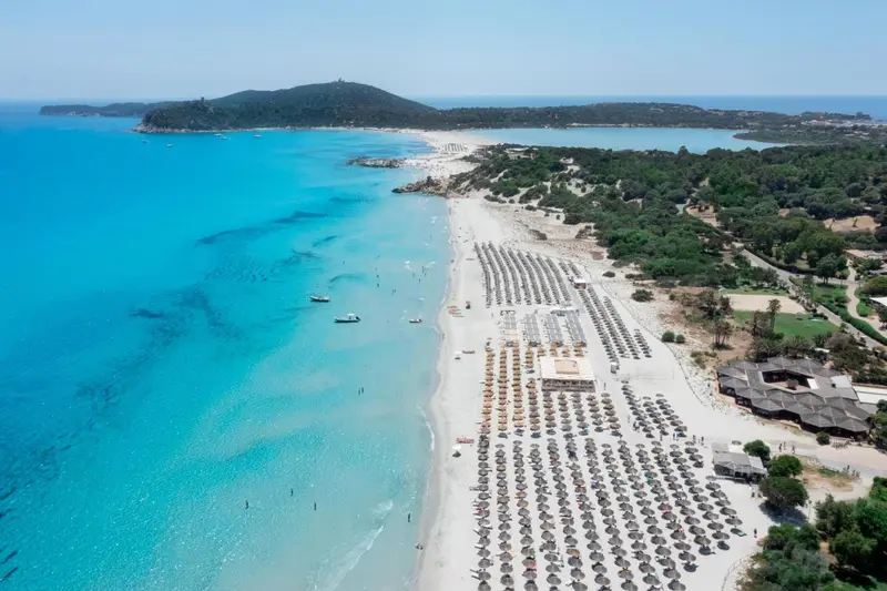 Vue aérienne d'une plage de sable fin bordée d'une eau turquoise et d'une végétation verdoyante.