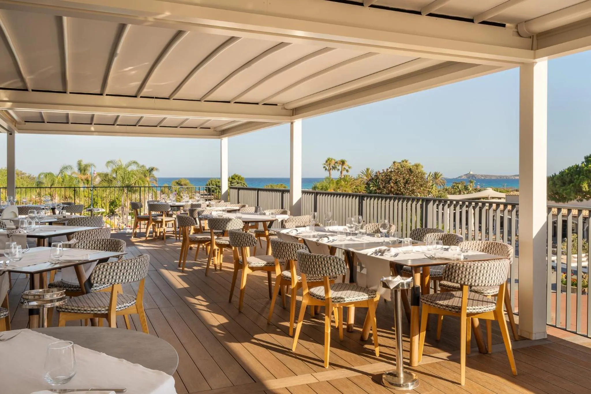 Terrasse ombragée avec tables et chaises donnant sur la mer.