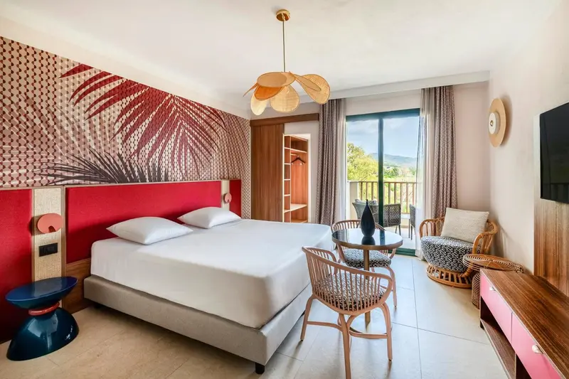 Une chambre lumineuse avec un lit double et un coin salon donnant sur une terrasse.