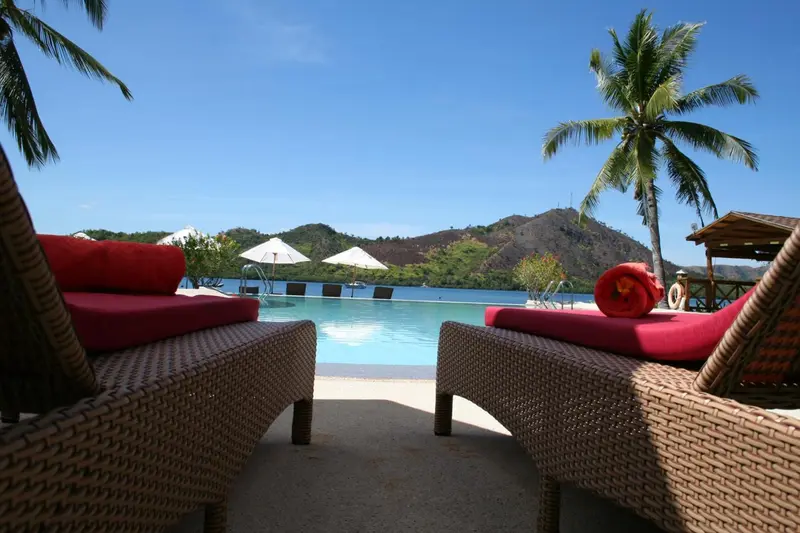Transats en rotin rouge et beige au bord d'une piscine turquoise.