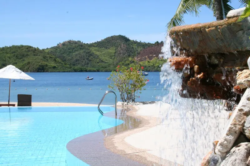 Une piscine bleue bordée d'une cascade rocheuse et de végétation tropicale.