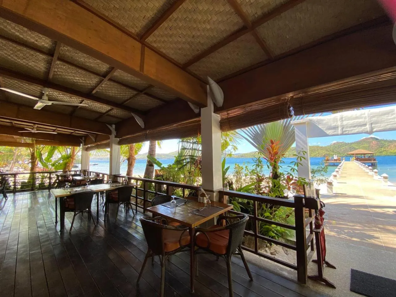 Terrasse ombragée avec tables et chaises donnant sur la mer.