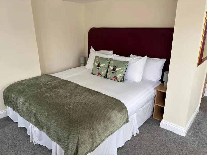 Une chambre lumineuse avec un grand lit recouvert d'une couverture verte et de coussins décoratifs.
