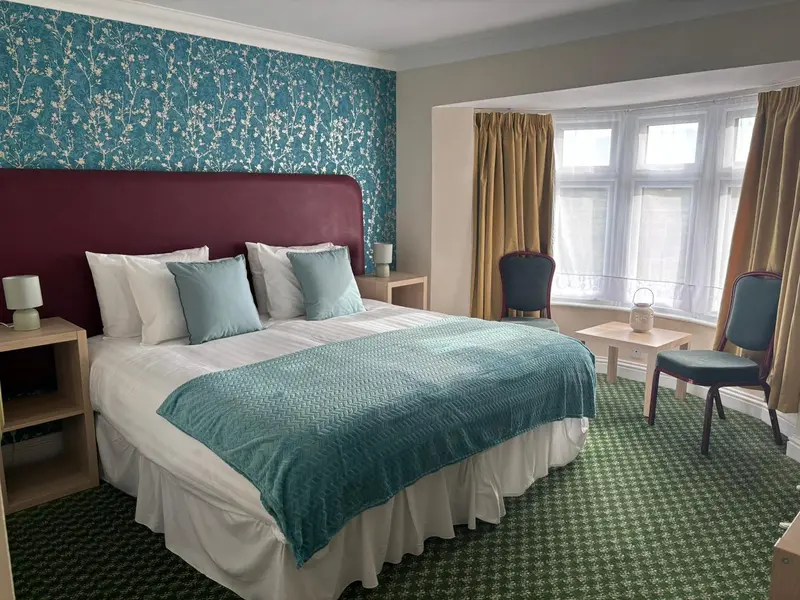 Une chambre lumineuse avec un grand lit recouvert d'une courtepointe turquoise et de coussins assortis.