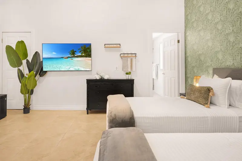 Une chambre lumineuse avec deux lits et une télévision diffusant une scène de plage.