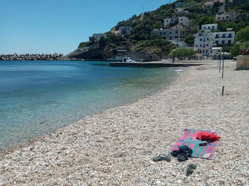 Plage de galets avec une eau turquoise et des bâtiments sur une colline.