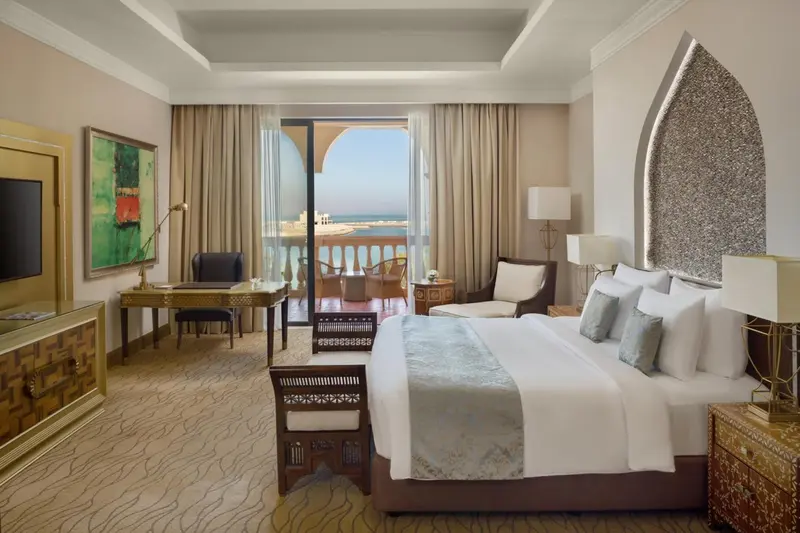 Chambre lumineuse avec un grand lit et une vue sur la mer depuis un balcon.