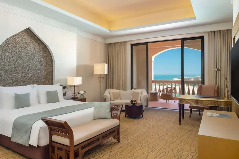 Chambre lumineuse avec un grand lit et un espace salon donnant sur une terrasse.