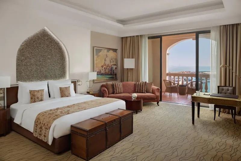 Une chambre lumineuse avec un grand lit et un coin salon donnant sur une terrasse.