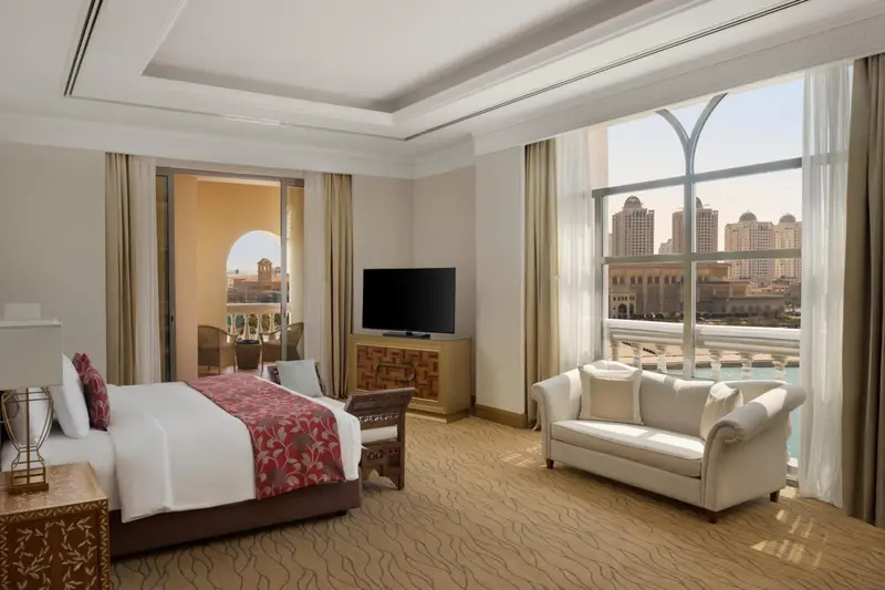 Une chambre lumineuse avec un grand lit et un coin salon donnant sur une vue urbaine.