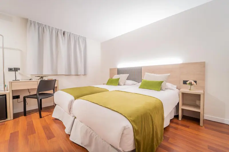 Une chambre lumineuse avec deux lits simples et un bureau.