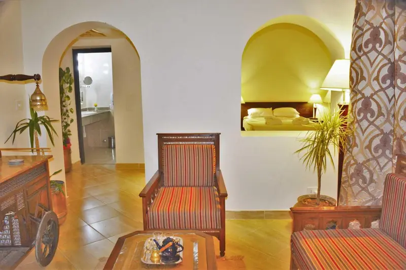 Espace de séjour lumineux avec mobilier coloré et ouvert sur une chambre.