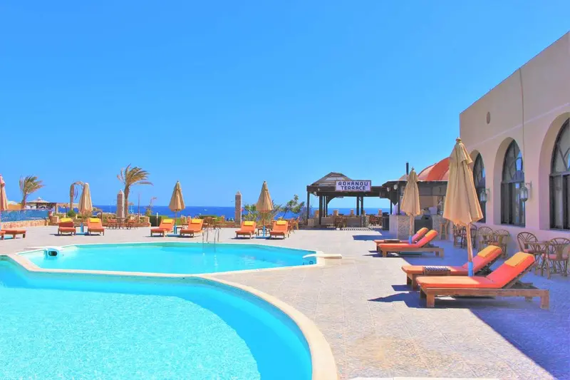 Transats oranges et bleus disposés autour d'une piscine turquoise sous un ciel bleu dégagé.