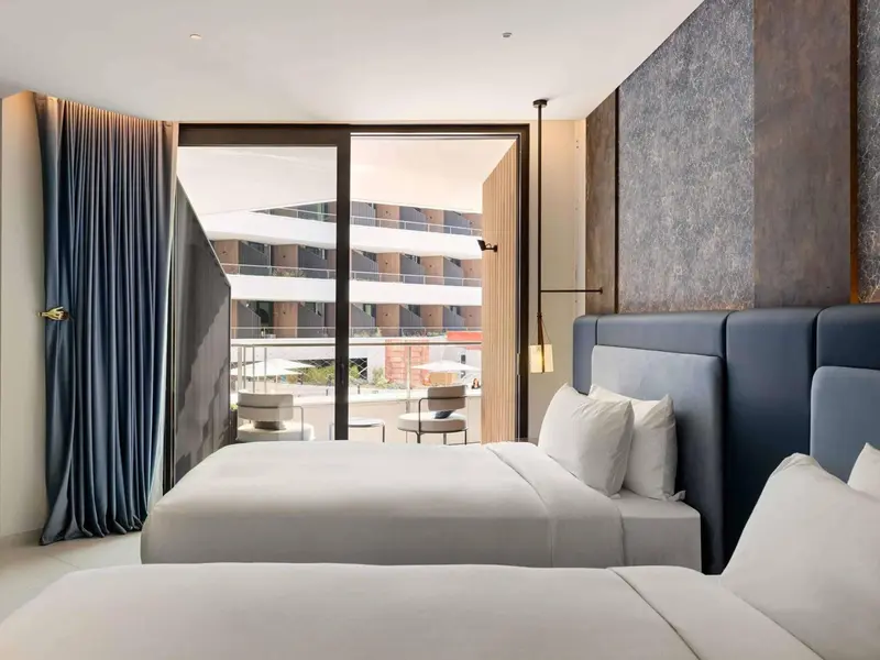 Une chambre lumineuse avec un grand lit et une vue sur un bâtiment moderne.