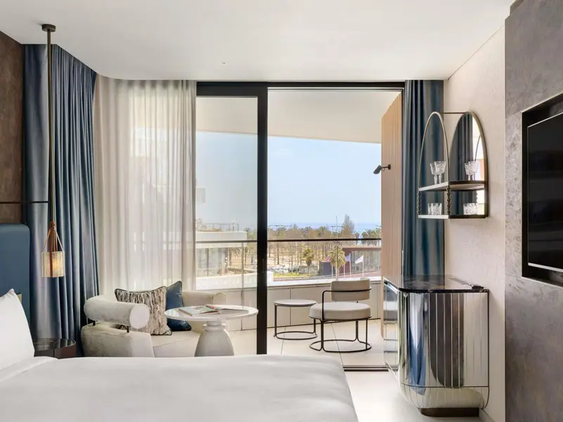 Chambre lumineuse avec un coin salon et vue sur la mer depuis un balcon.